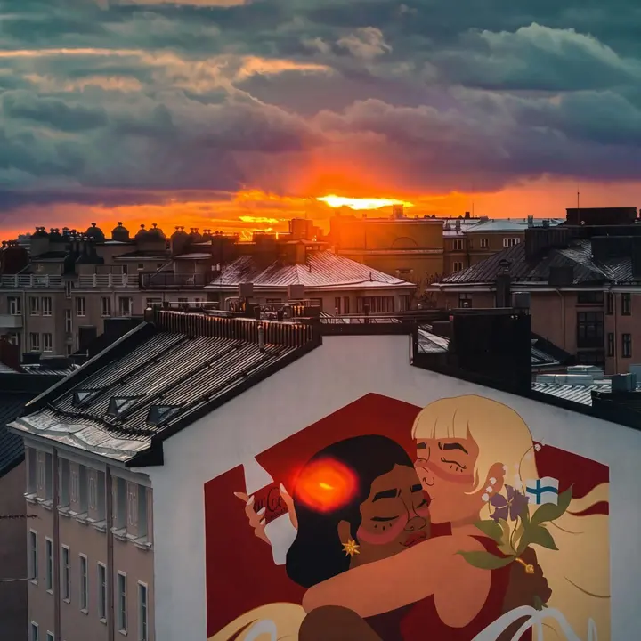 Auringonlasku Kallion kattojen ja suuren seinämaalauksen yllä