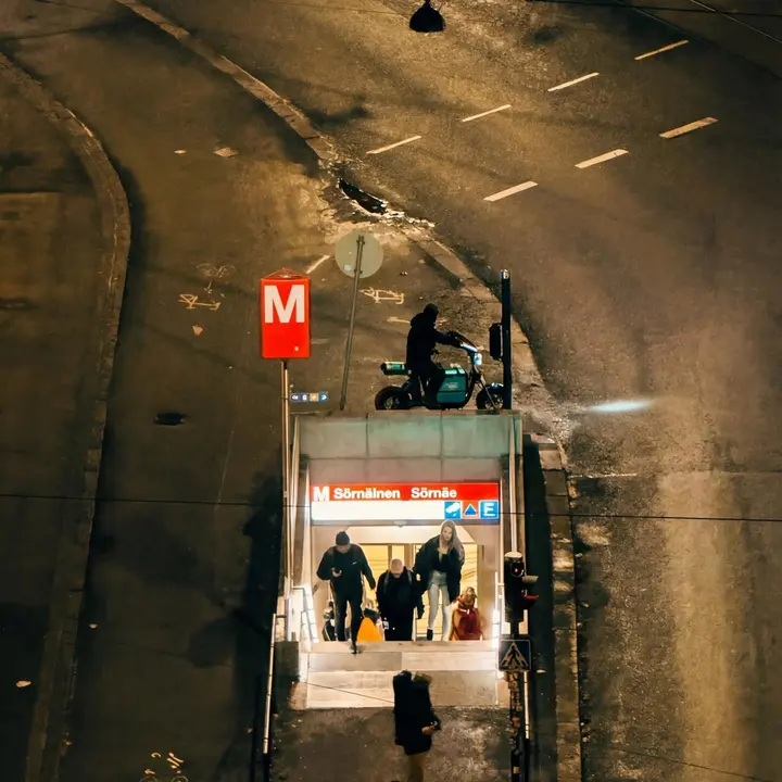 Sörnäisten metroaseman sisäänkäynti ja kadulla liikkuvia ihmisiä yöllä